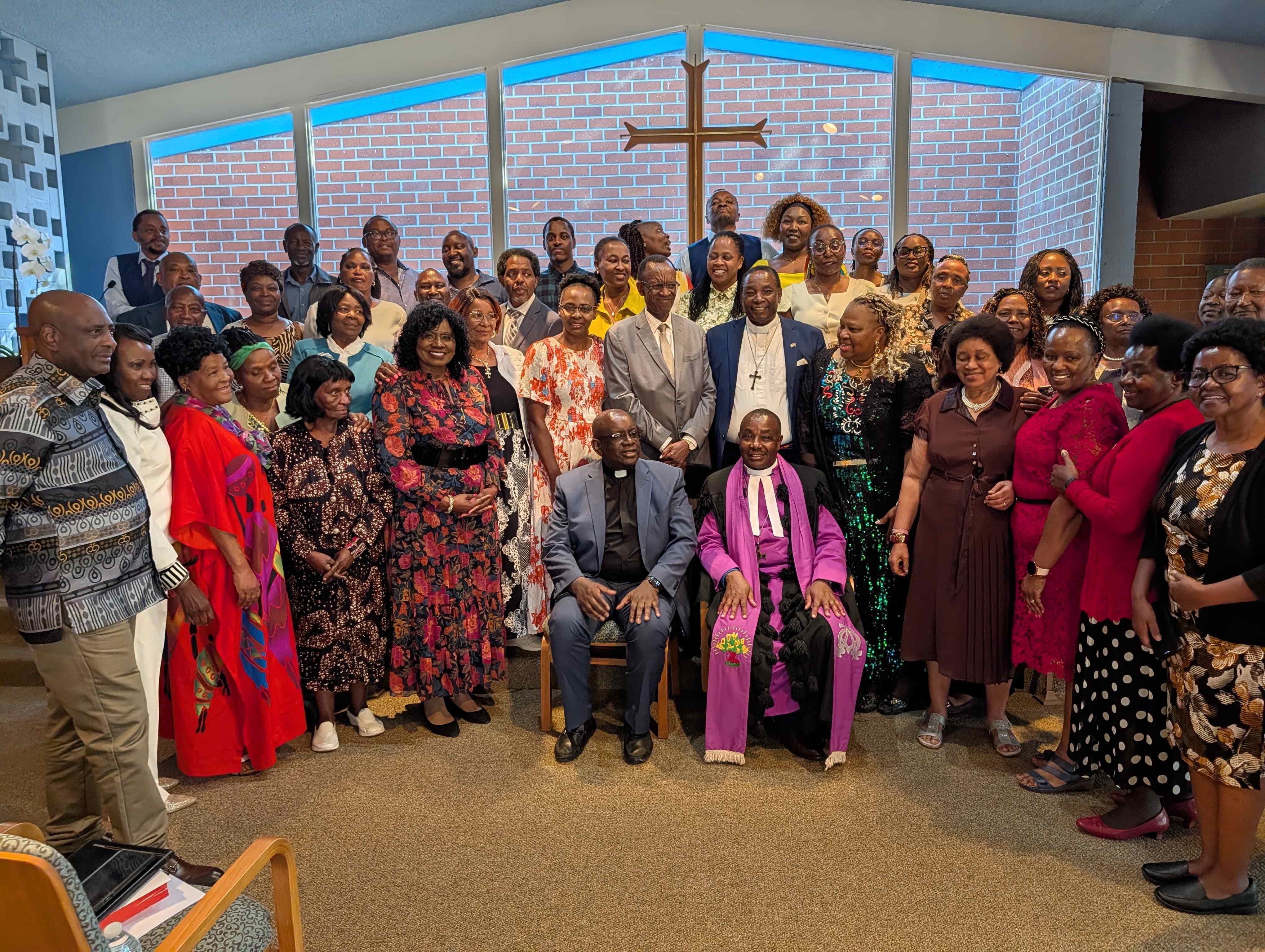 CAGI congregation gathered in worship, with church leaders seated in front and the community standing together beneath a wooden cross